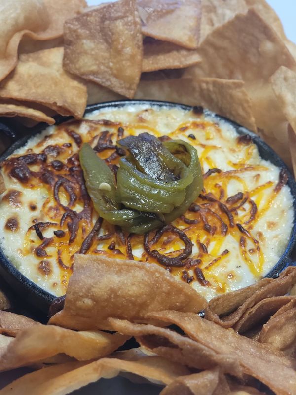 Queso dip with tortilla chips, topped with grilled onions and jalapeño.