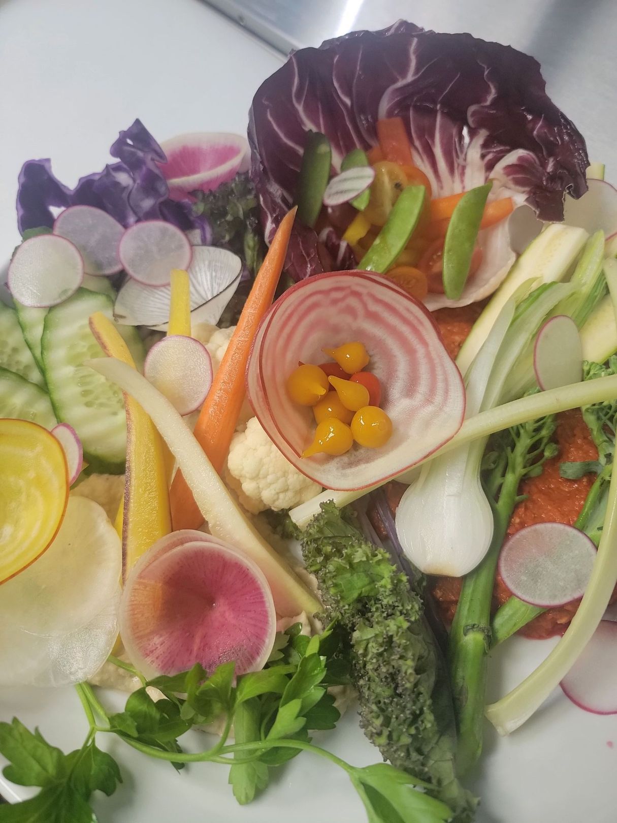 fresh vibrant vegetables on a plate with hummus and romesco sauce and pita bread