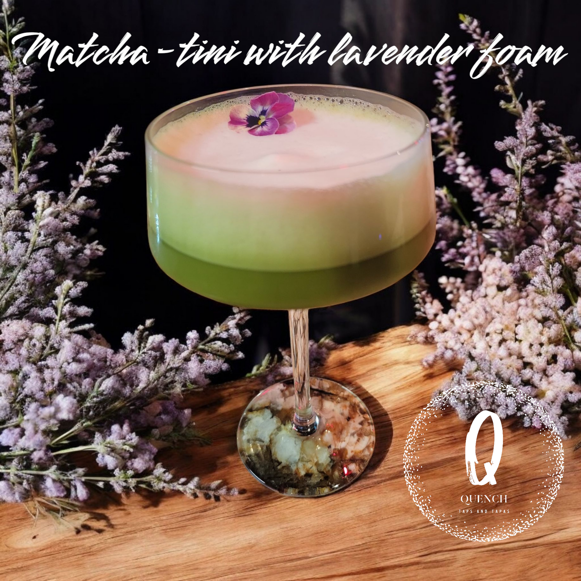 Matcha-tini with lavender foam cocktail in a glass, surrounded by flowers on wood.