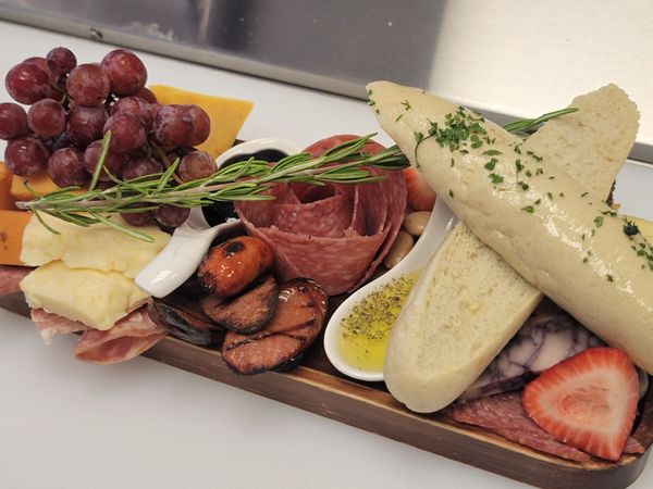 Charcuterie board with grapes, cheese, meats, bread, and a sprig of rosemary.