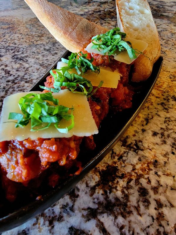 Meatballs in tomato sauce topped with cheese and basil, served with bread.