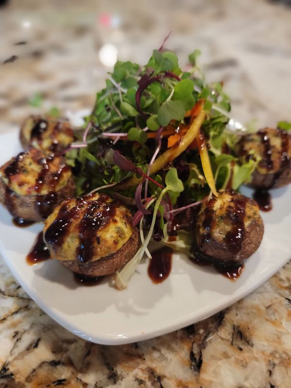 Stuffed mushrooms drizzled with balsamic glaze, served with a salad on a white plate.
