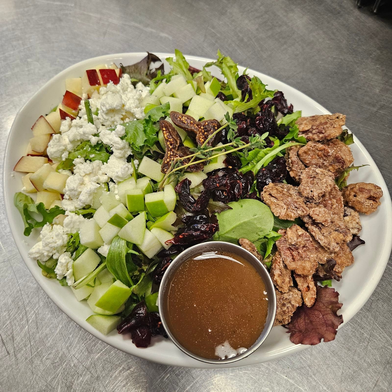 Salad with apples, goat cheese, candied pecans, and vinaigrette on a white plate.