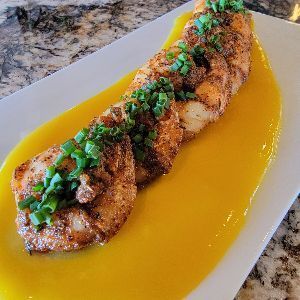 Seared seafood dish with mango sauce, garnished with green onions on a white plate.