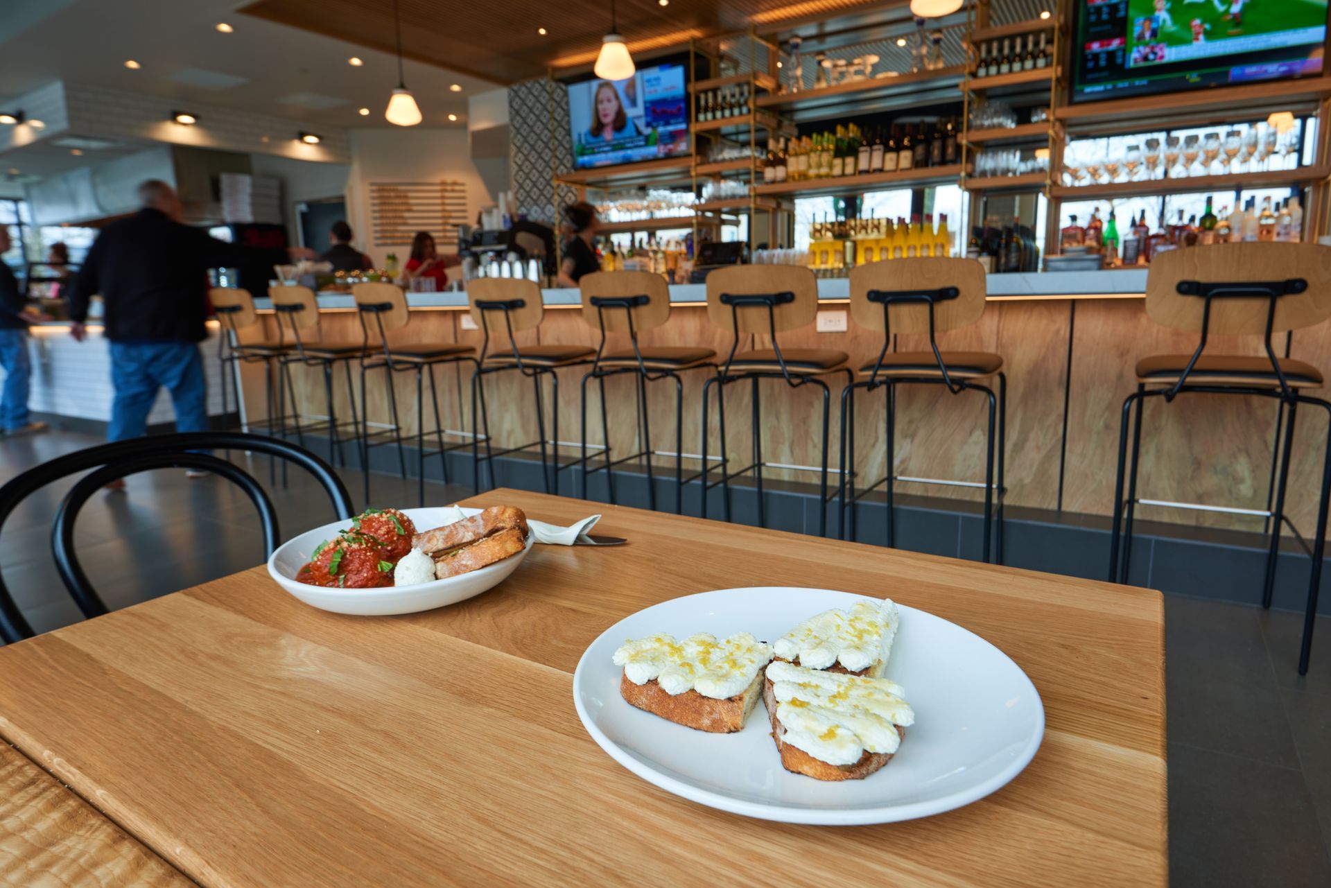 Two plates of food are on a wooden table in a restaurant.