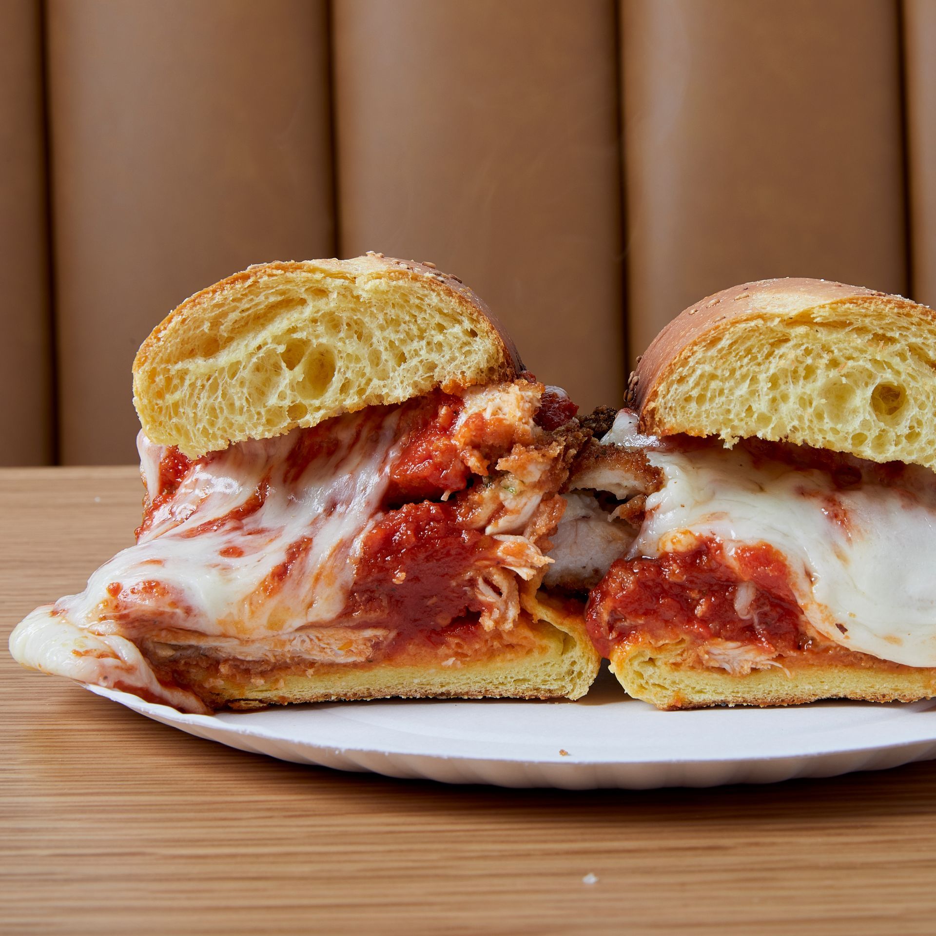 A chicken parmesan sandwich is cut in half on a white plate.