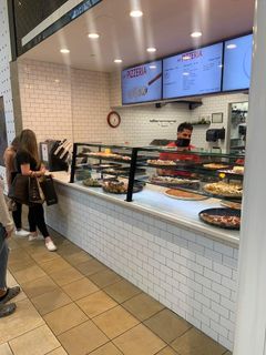 A man is standing behind a counter at a pizza restaurant.