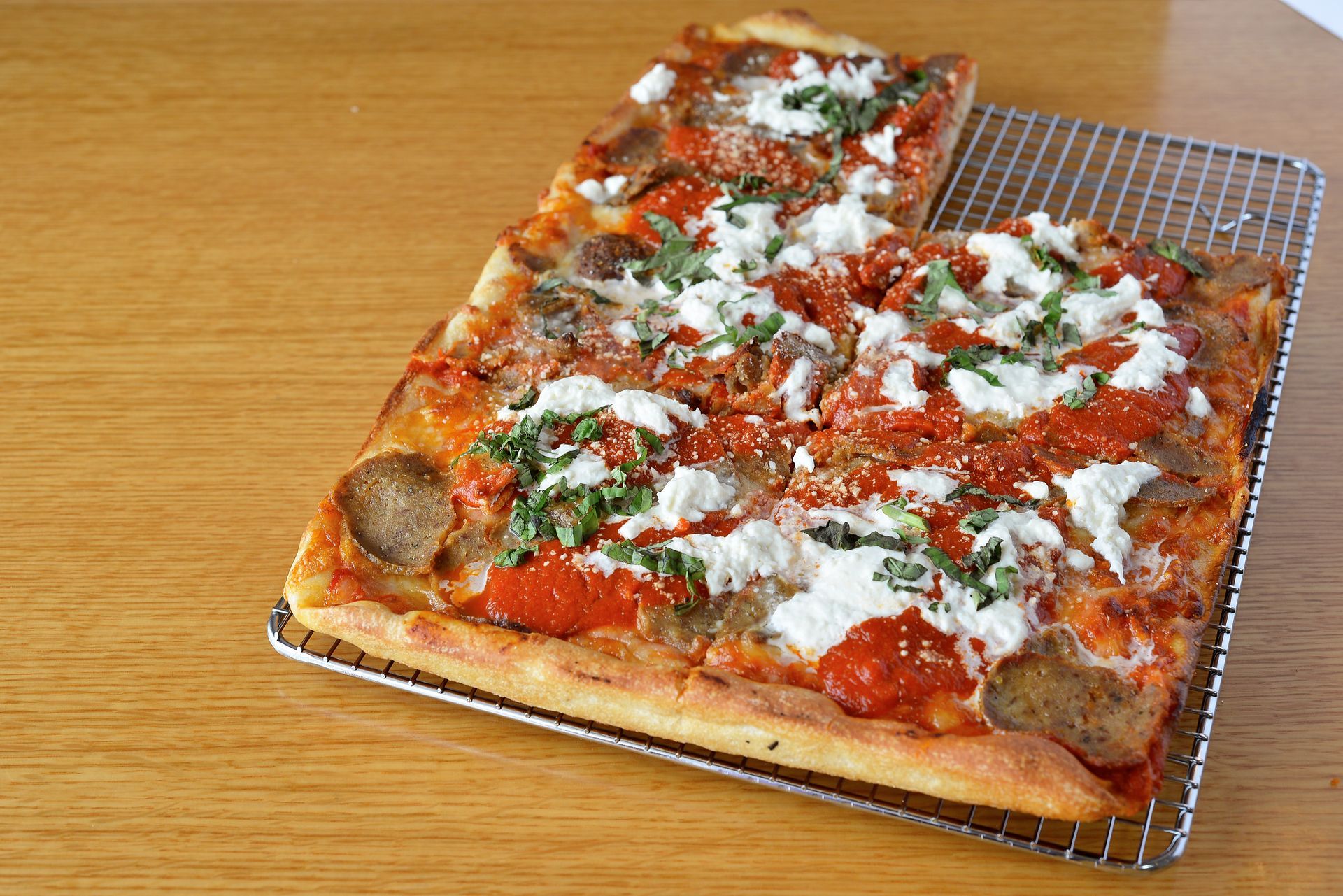 A pizza is sitting on a wire rack on a wooden table.