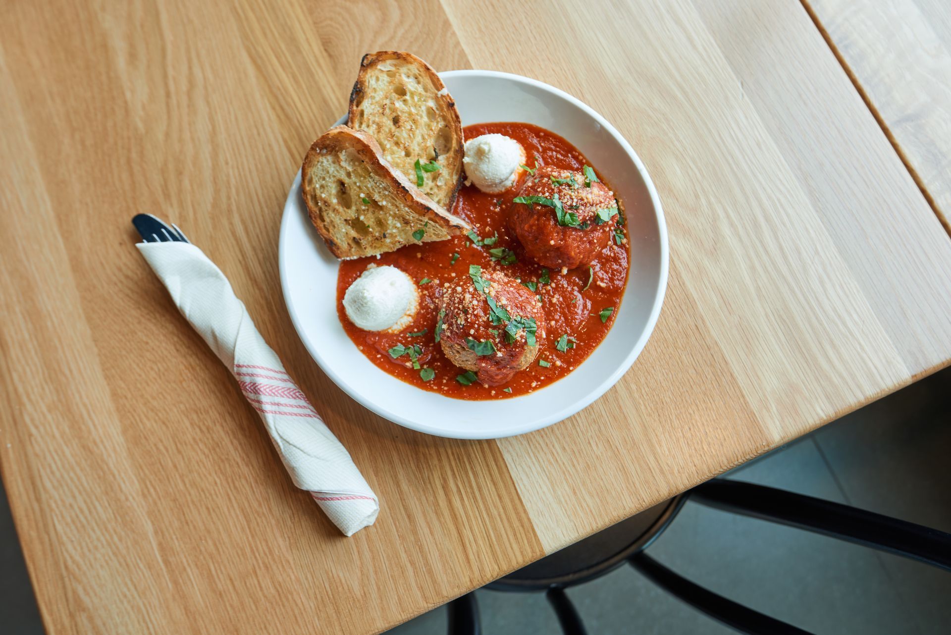 A bowl of meatballs and bread on a wooden table.