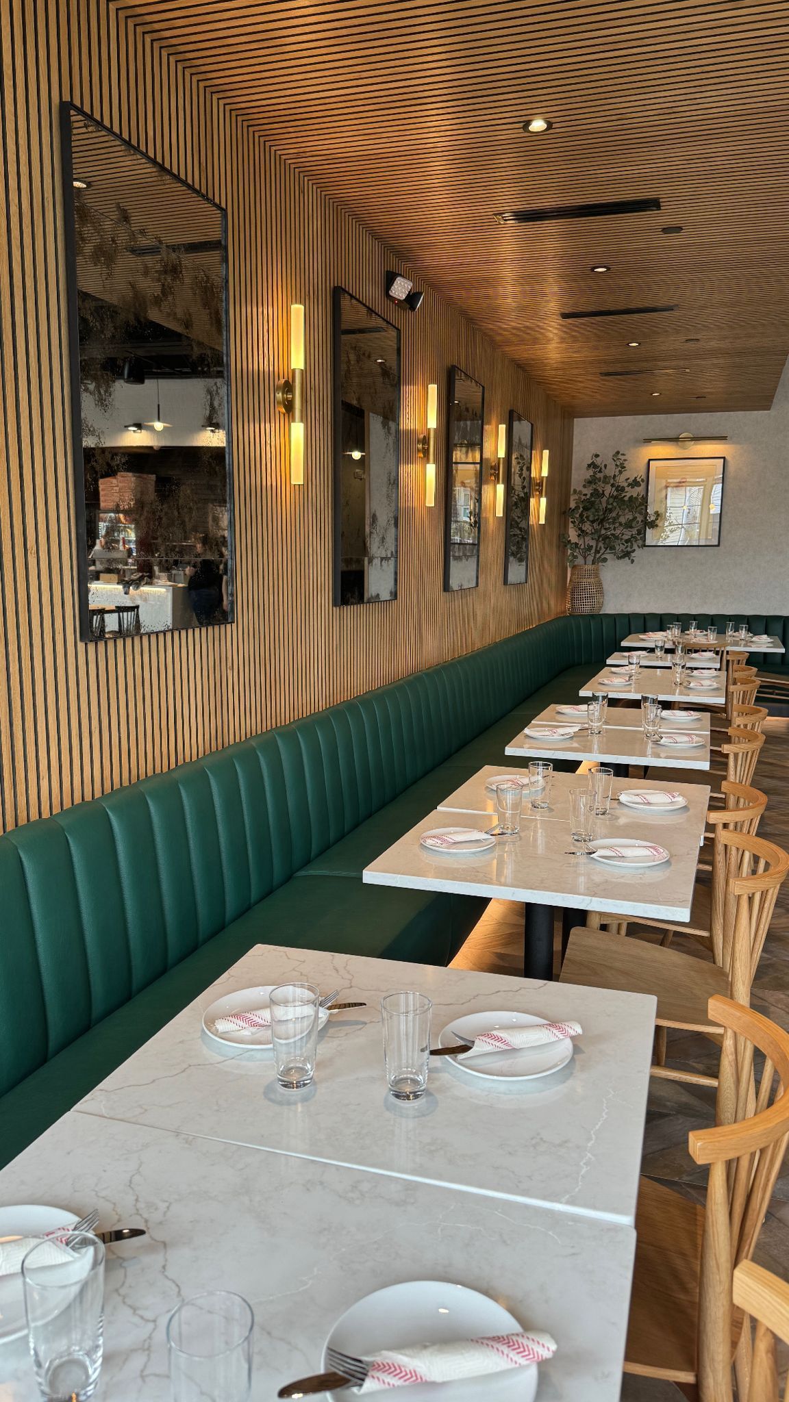 A long dining room with tables and chairs and a green bench.