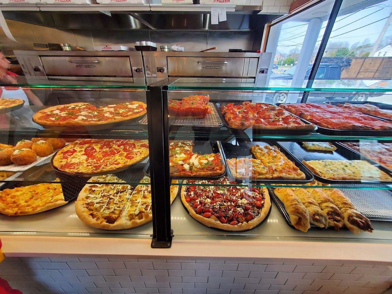 A variety of pizzas are displayed in a glass case in a restaurant.