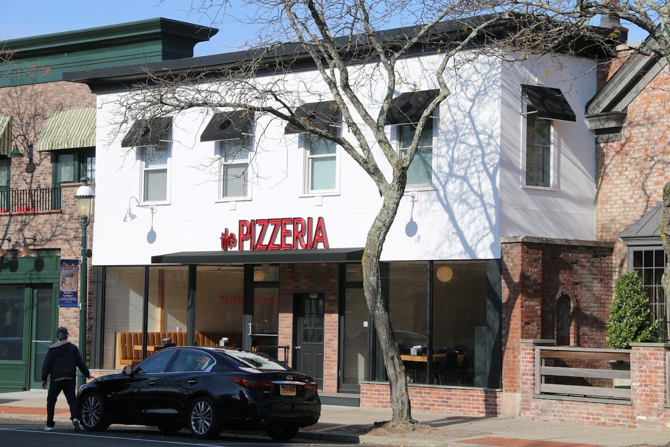 A black car is parked in front of a pizzeria.