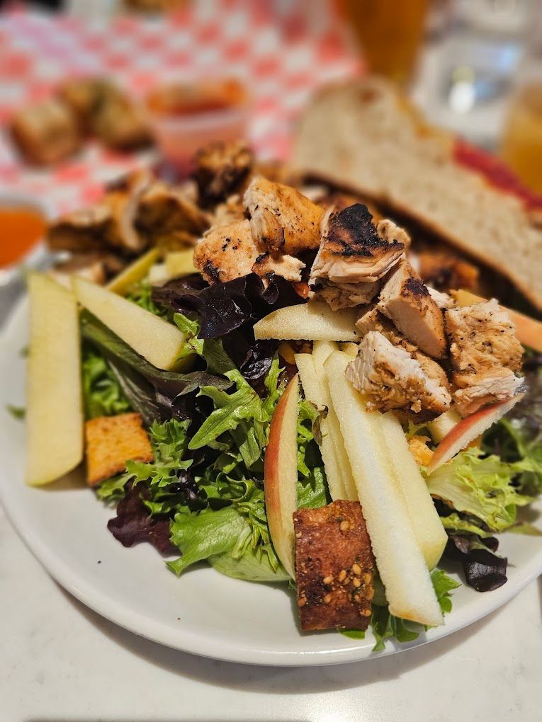 A salad with chicken , apples , and lettuce on a white plate.