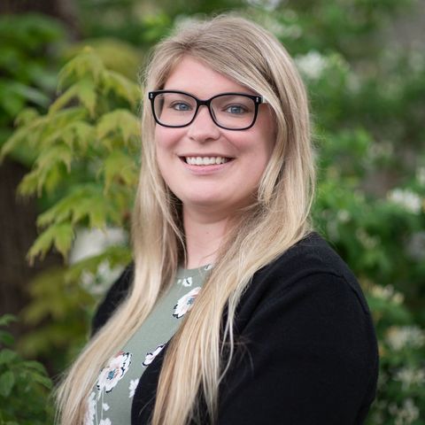 A woman wearing glasses and a black sweater is smiling for the camera.