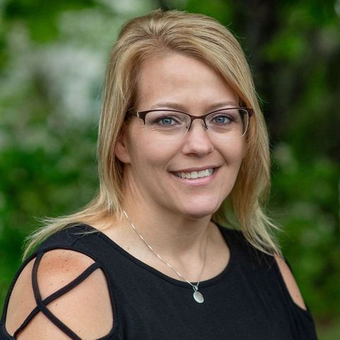A woman wearing glasses and a black shirt is smiling for the camera.