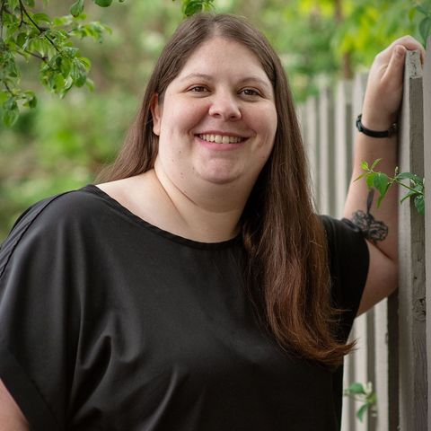 A woman in a black shirt is leaning against a wooden fence and smiling.