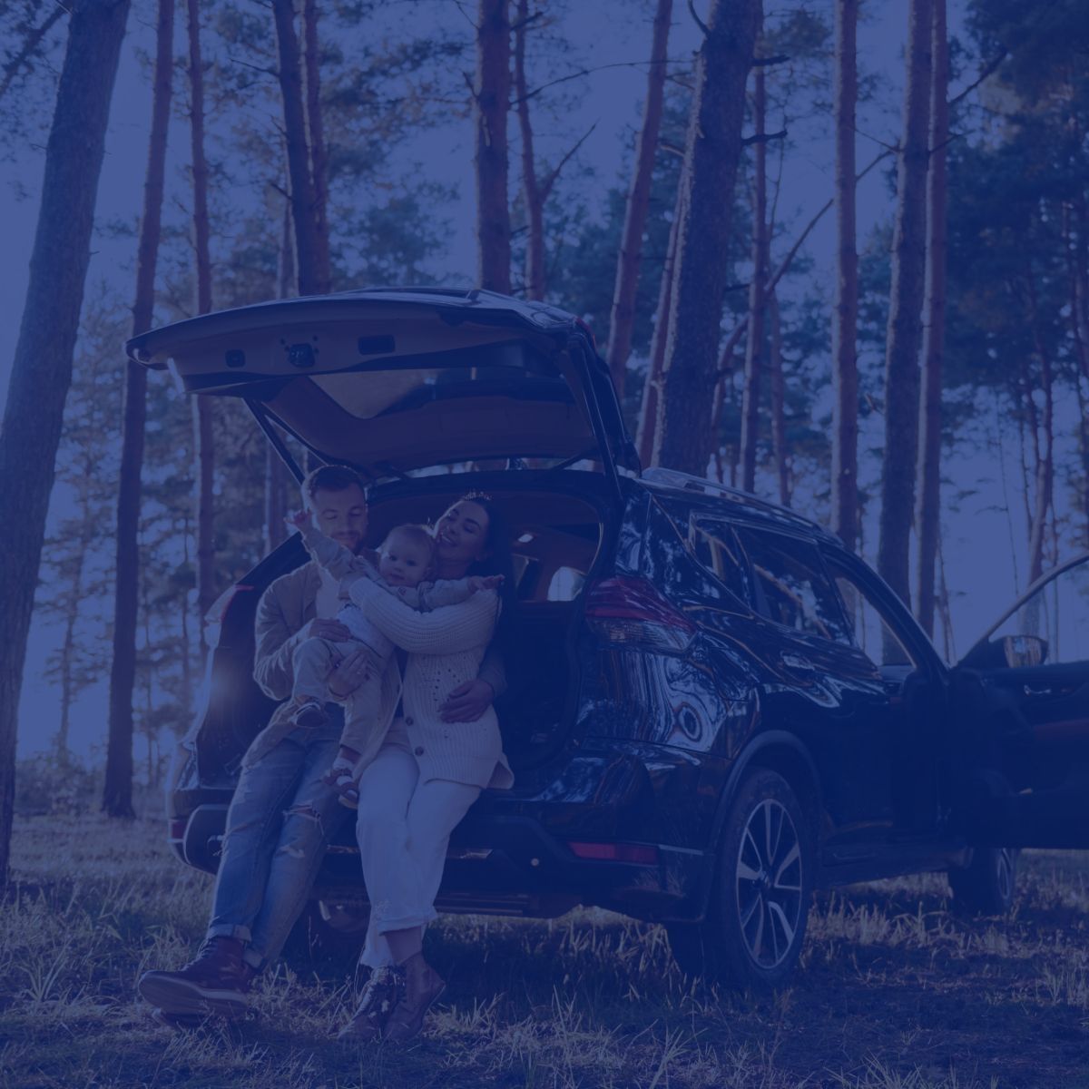 A family is sitting in the back of a car in the woods.