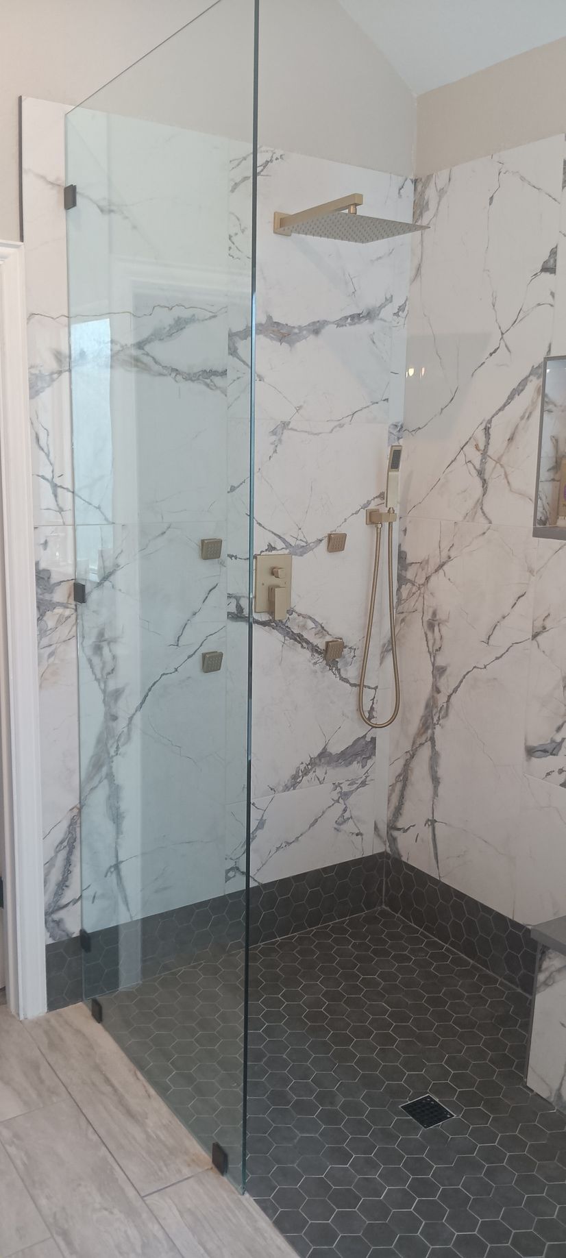A modern bathroom with a white vanity, a toilet, and a glass-enclosed shower against light grey tiled walls.
