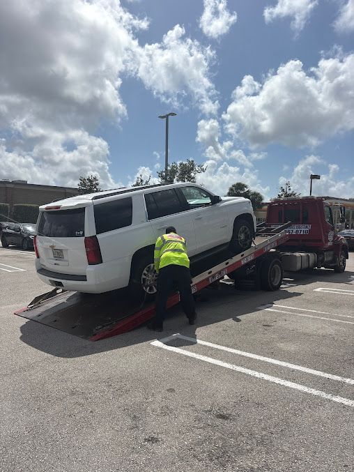 A white suv is being towed by a tow truck in a parking lot.