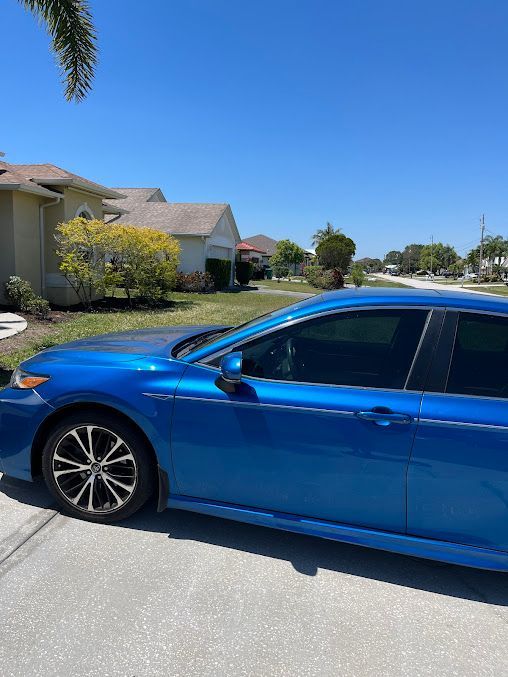 A blue car is parked on the side of the road in front of a house.