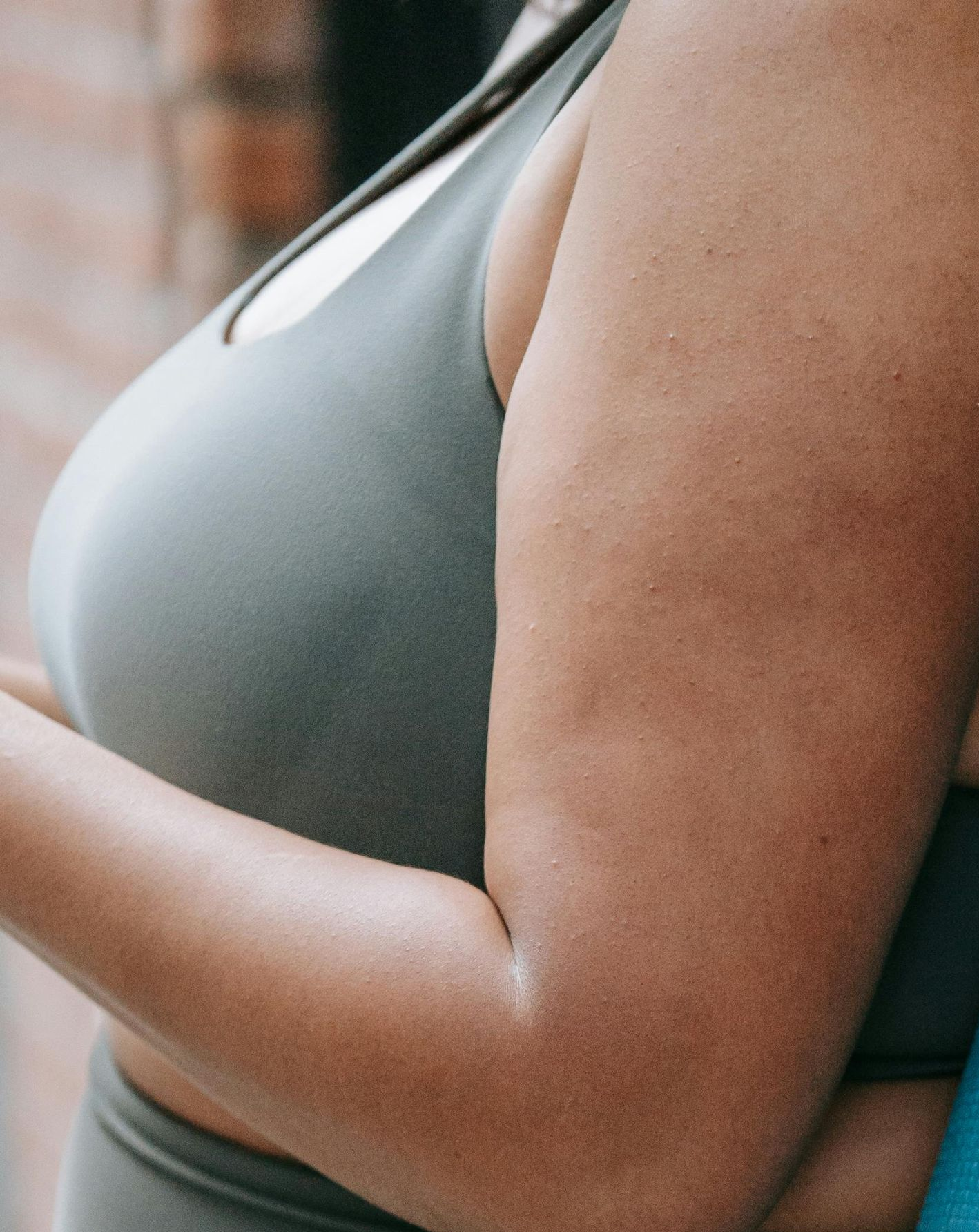 Woman wearing a gray sports bra, side view, arm extended, against a blurred background.