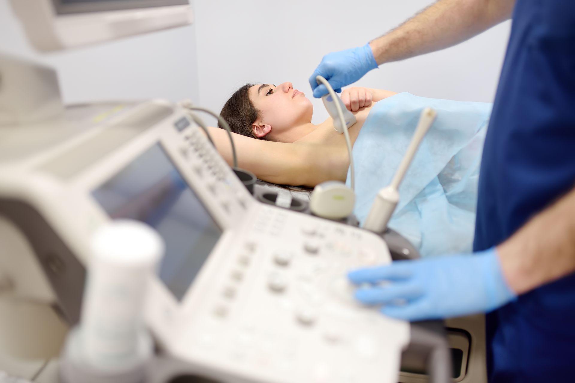 Woman undergoing ultrasound scan in a medical setting. Doctor uses probe on chest, blue gloves.