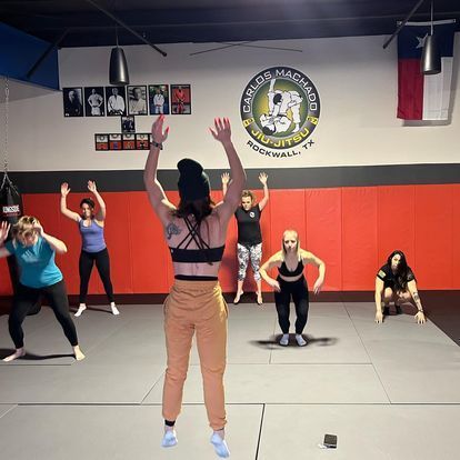 A group of people are doing exercises in a gym with a sign that says ' texas mma ' on it