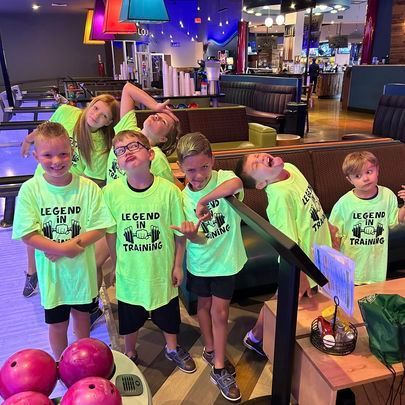 a group of children wearing neon green shirts are posing for a picture in a bowling alley .