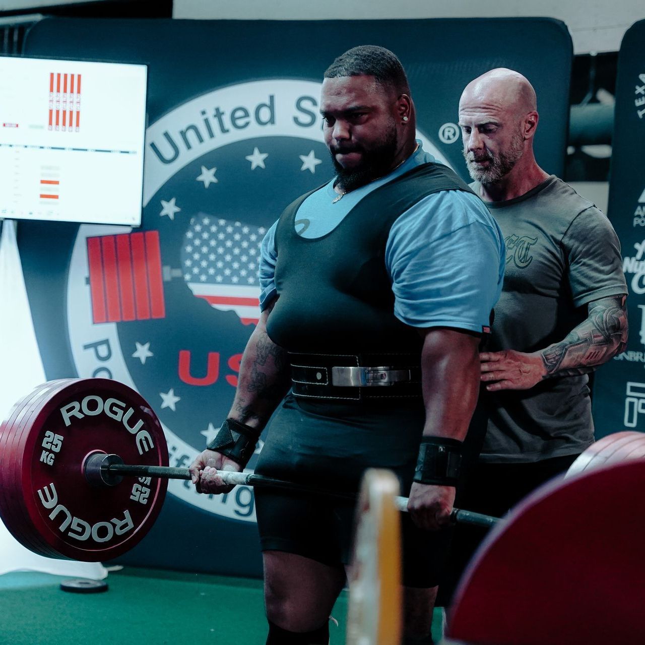 A man lifting a barbell in front of a sign that says united states