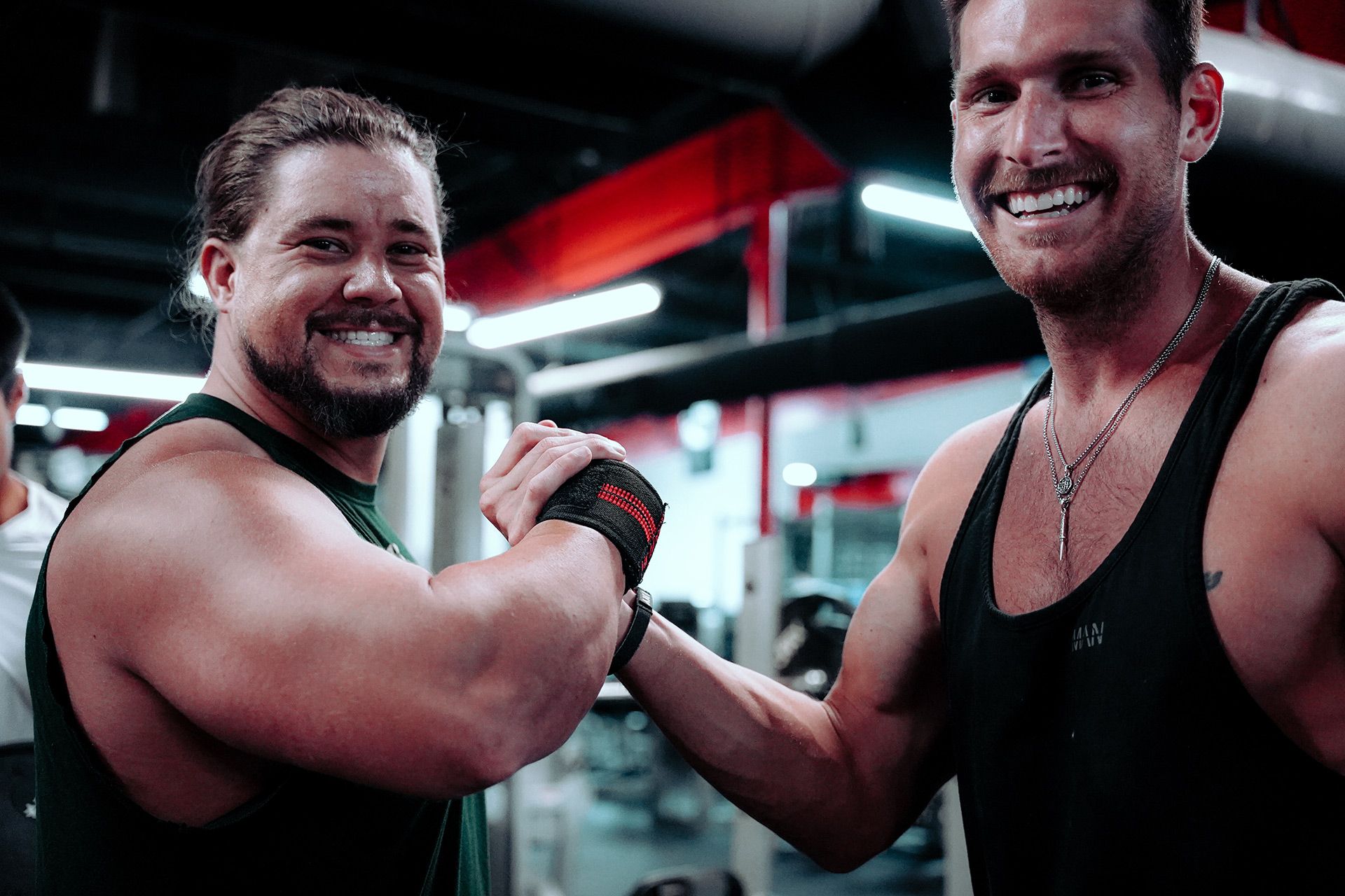 Two men are shaking hands in a gym and smiling.