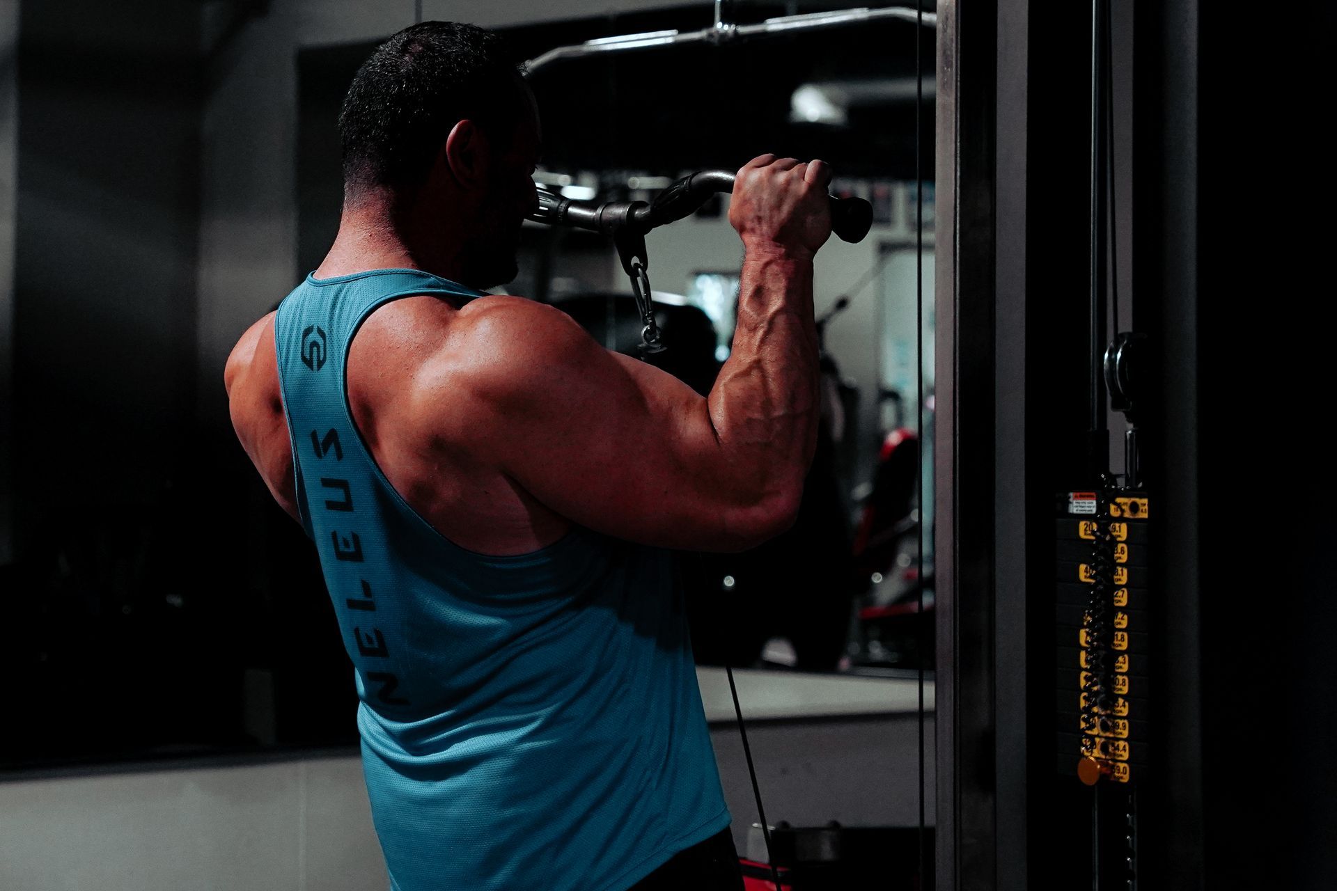 A man in a blue tank top is using a machine in a gym.