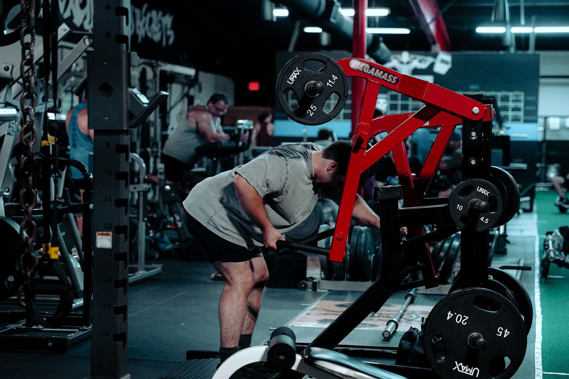 A man is squatting on a machine in a gym.