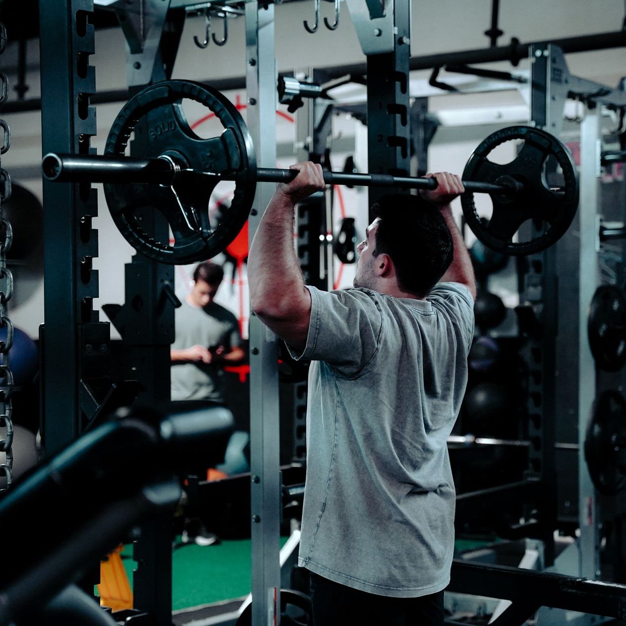 A man is lifting a barbell over his head in a gym