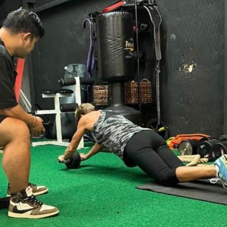 A man is sitting next to a woman doing push ups in a gym.