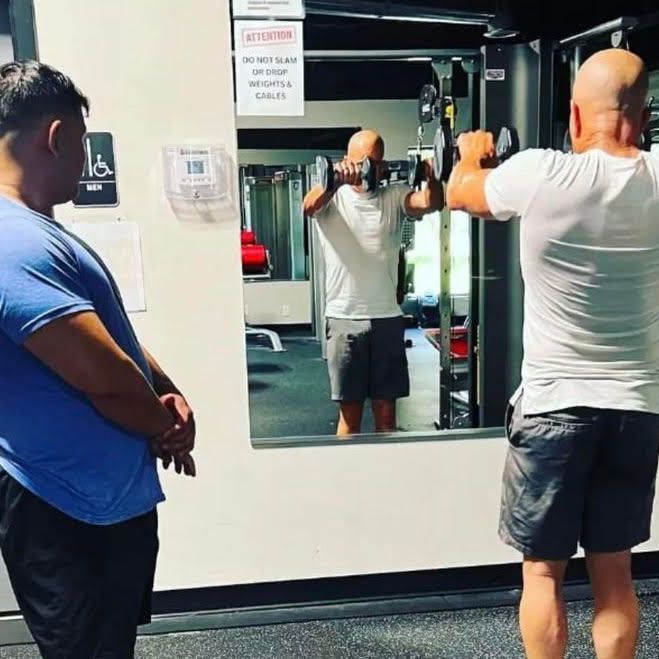 A man in a blue shirt is looking at another man in a gym