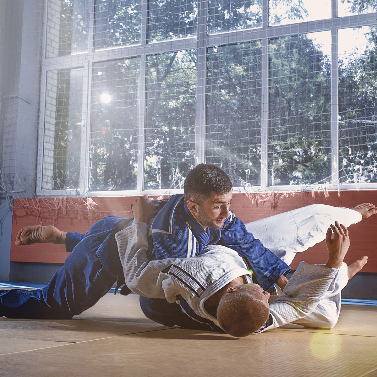 Two men are practicing judo on the floor in a gym.