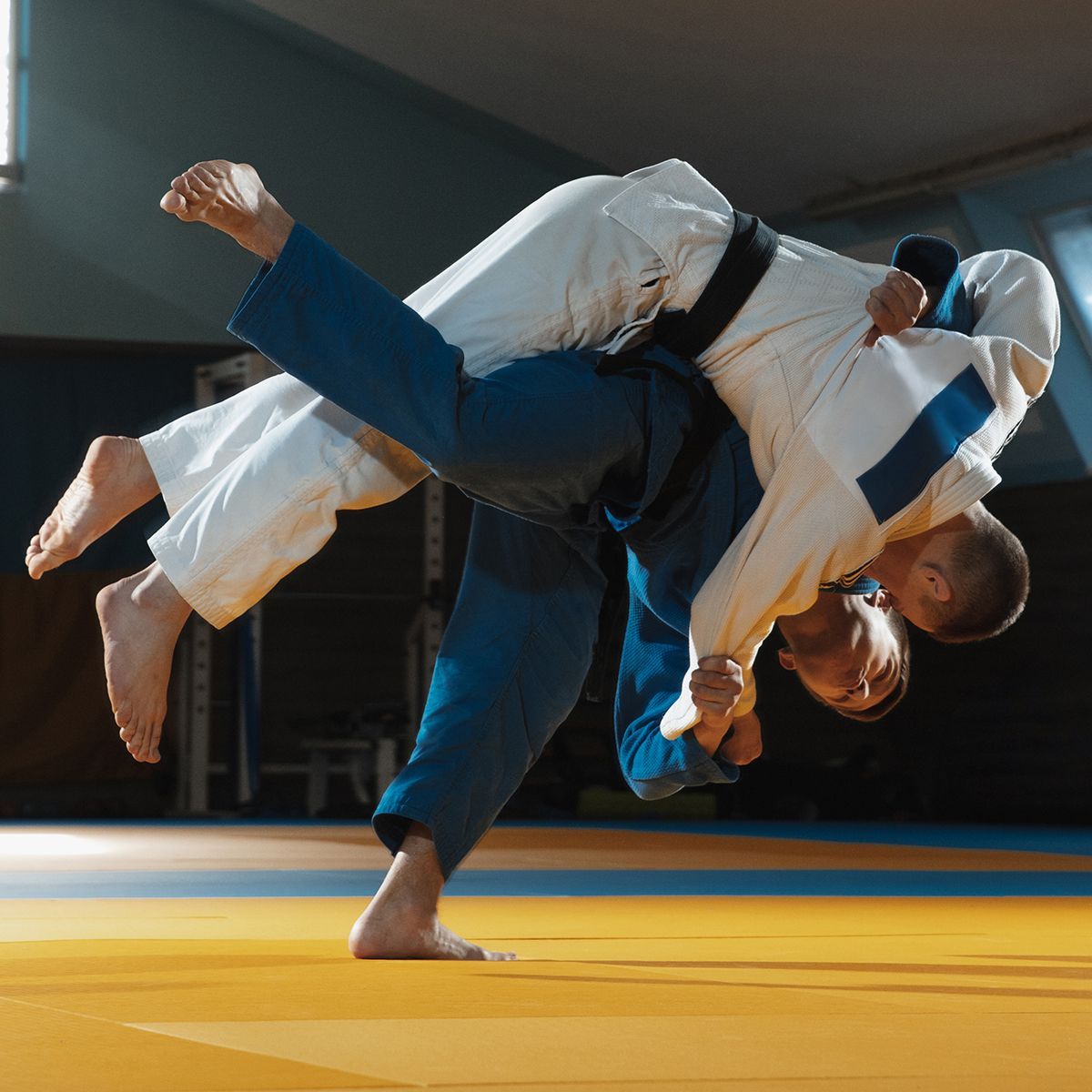 Two men are practicing judo on a mat in a gym.