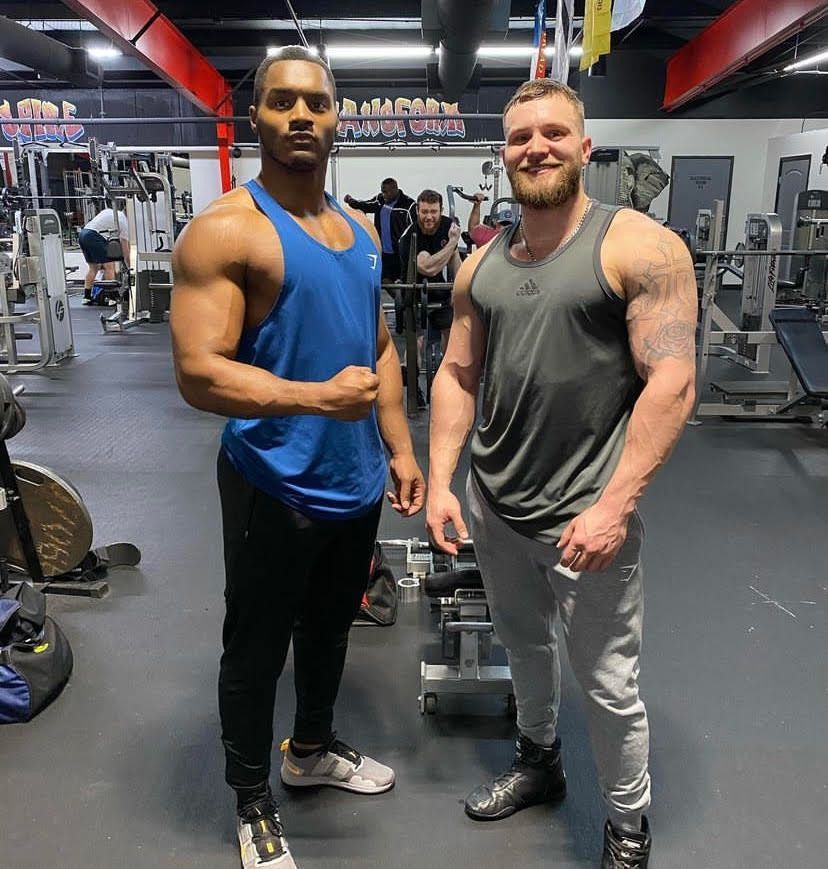 Two men are posing for a picture in a gym