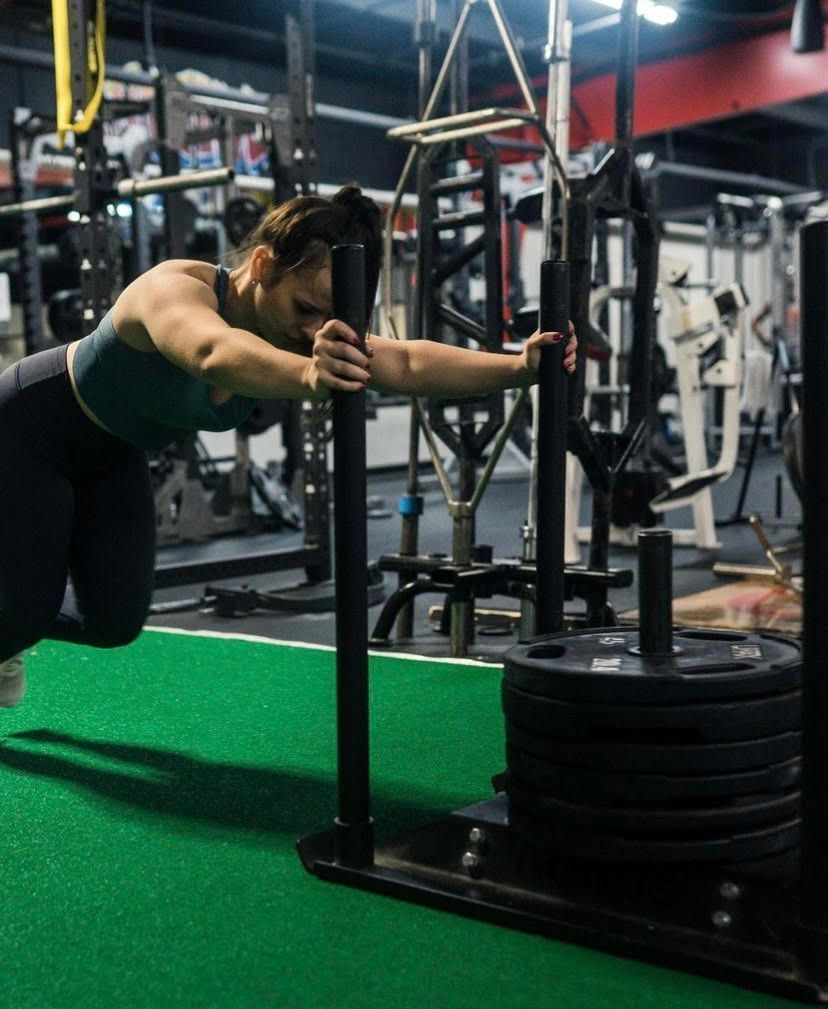 A woman is doing push ups on a sled in a gym.