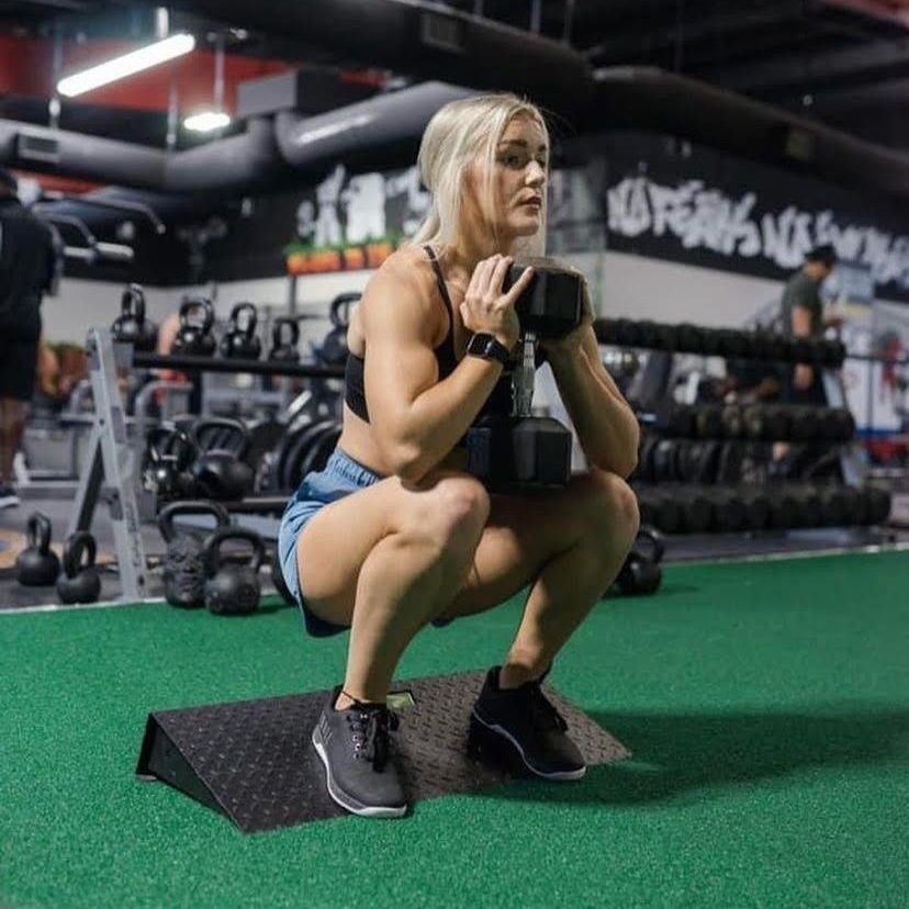 A woman squatting with a dumbbell in a gym