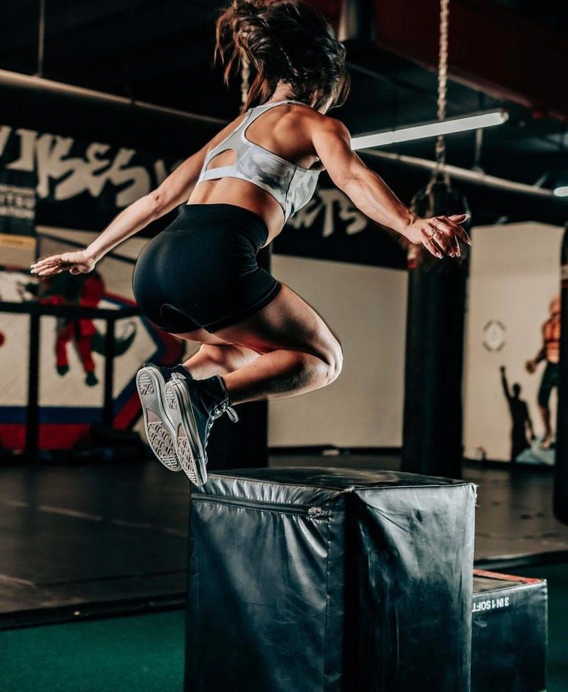 A woman is jumping over a box in a gym.
