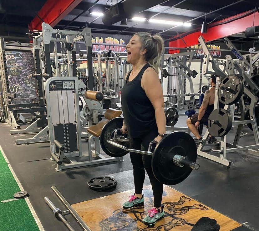 A woman is lifting a barbell in a gym.