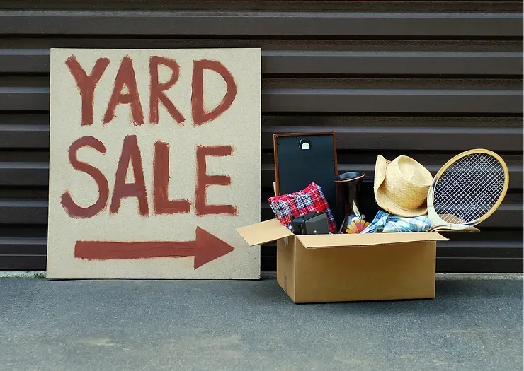 A yard sale sign is next to a cardboard box filled with items.