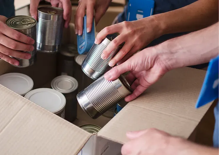 A group of people are putting cans into a cardboard box.