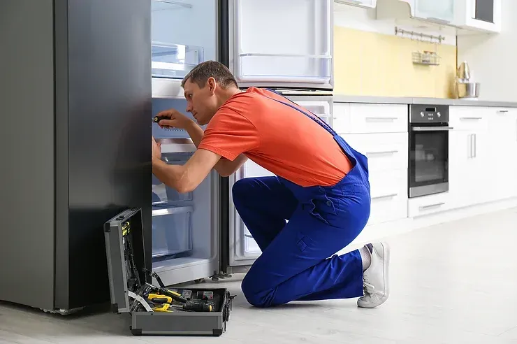 A man is repairing a refrigerator in a kitchen.