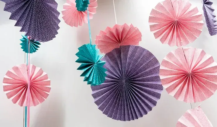A bunch of paper fans hanging from a string on a wall.