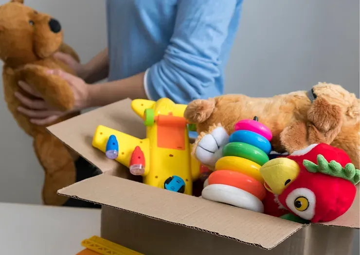A person is putting stuffed animals in a cardboard box.