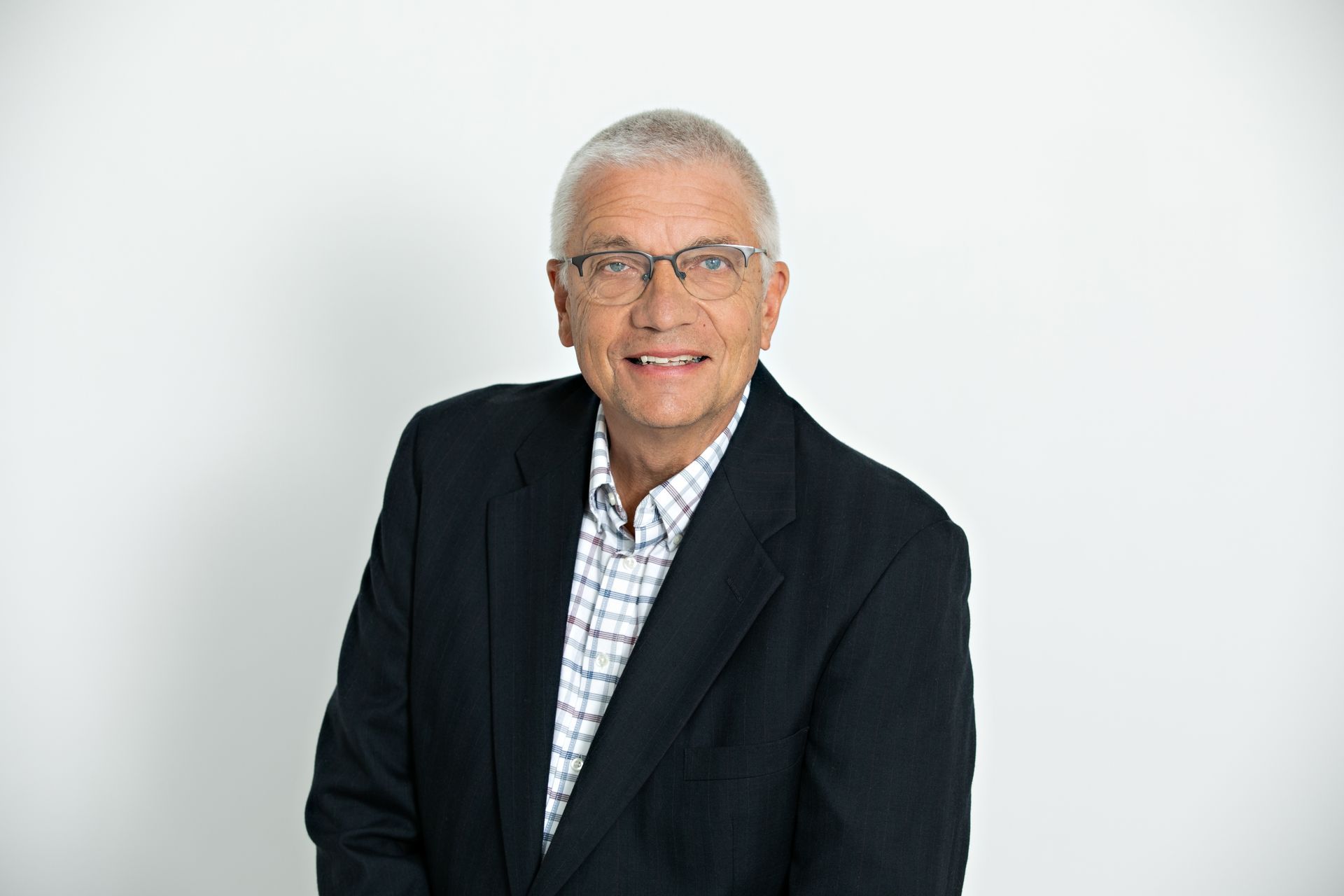 Man with glasses, arms crossed, wearing a maroon shirt with a logo, smiling, neutral background.