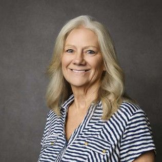 Woman with long blonde hair, smiling, wearing a striped blue and white shirt. Against a gray backdrop.