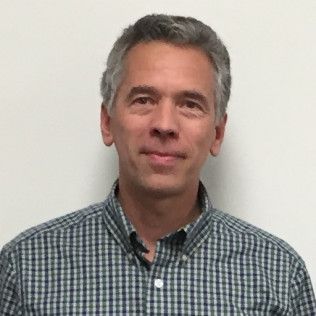 Man with graying hair wearing a blue and gray plaid shirt.